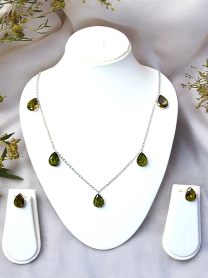 An olive green Swarovski crystal teardrop necklace with matching stud earrings displayed on a mannequin against a floral background.